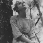 Woman in forest gazes upwards, serene and thoughtful.