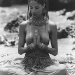 Woman meditating on beach, wearing intricate jewelry.