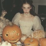 Person in vintage dress with pumpkins and Halloween decor.
