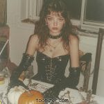 Woman in gothic costume with pumpkins on table.