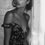 Woman in floral dress by window, black and white.