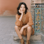 Woman in brown dress sitting by tiled wall