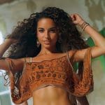 Woman posing with curly hair and patterned top.