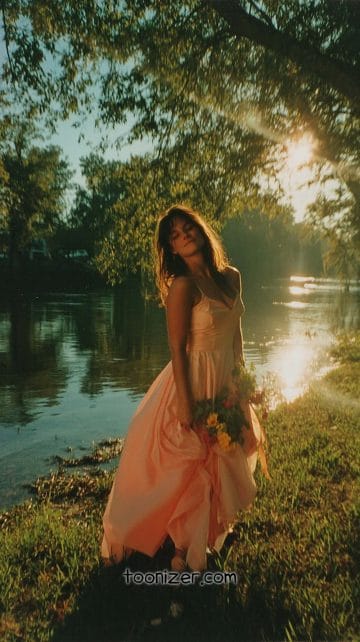 Woman in pink dress by river at sunset.