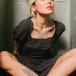Woman with tattoos sitting cross-legged in a room.