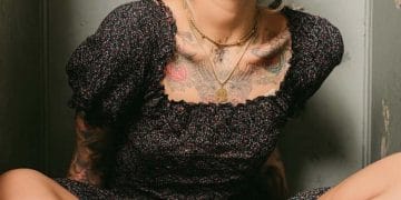 Woman with tattoos sitting cross-legged in a room.