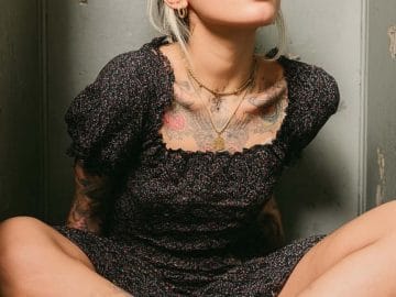 Woman with tattoos sitting cross-legged in a room.