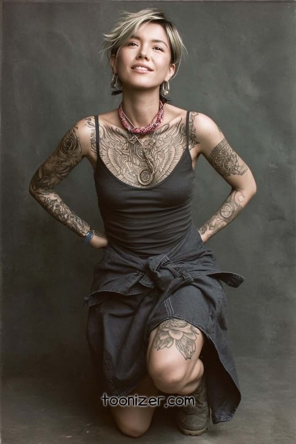 Tattooed person smiling, kneeling on one knee.