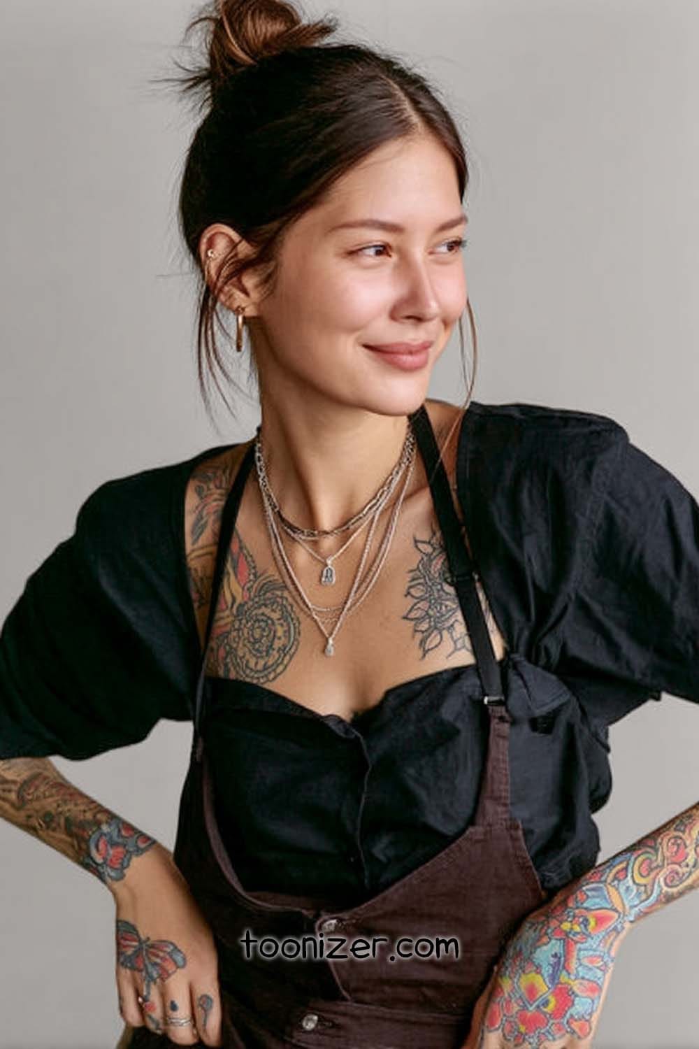 Smiling woman with tattoos and layered necklaces.