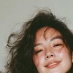 Smiling woman wearing patterned dress and tousled hair.