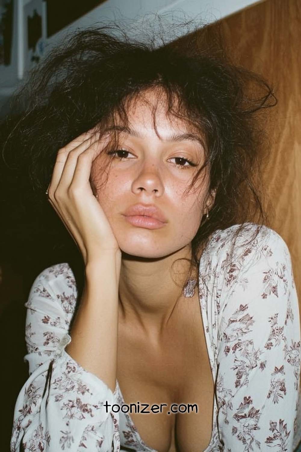 Woman leaning on hand, floral blouse, thoughtful expression.