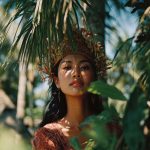 Woman in crown surrounded by tropical leaves.