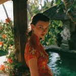 Woman in red dress by tropical poolside.