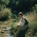 Person sitting by a serene forest stream.