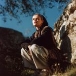 Person in nature, crouching near rocks and trees.