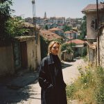 Person in long coat on sunny alley.