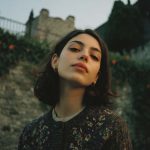 Woman poses confidently outdoors, ancient stone wall background.