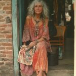 Elderly woman in colorful bohemian attire sitting outside.