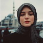 Woman with headscarf, blurred city background.