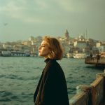Woman gazes over city waterfront at sunset.