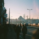 People walking on bridge towards mosque at sunset.