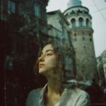 Woman reflecting through window, historic tower in background.