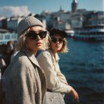 Two women by waterfront, city skyline background.