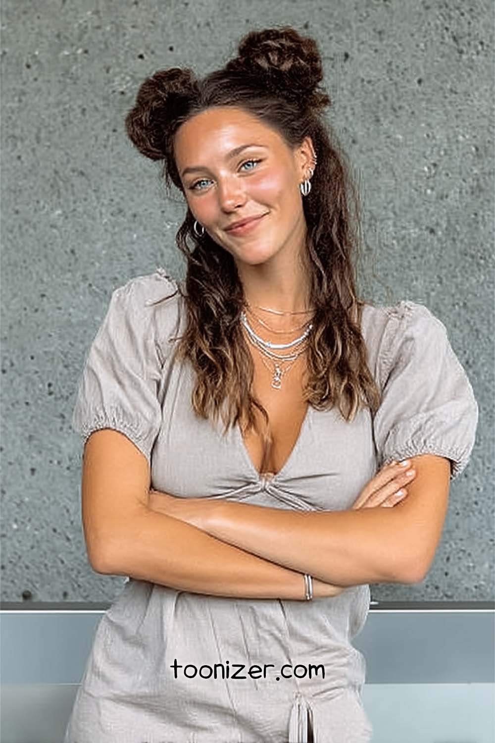 Smiling person with crossed arms against gray wall.