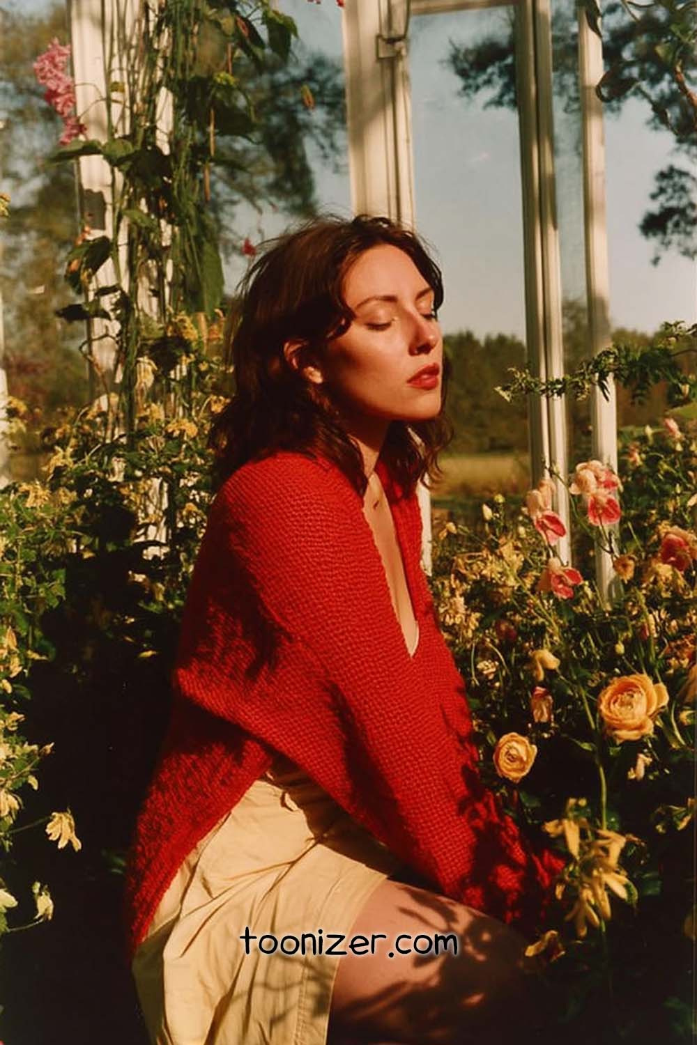 Woman in red sweater near flowers outside.