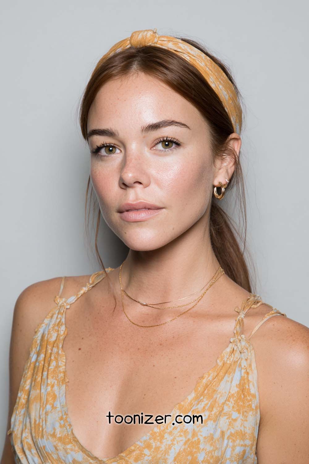 Woman with headband and gold necklace smiling slightly.