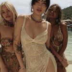 Three women in beachwear standing by the shore.