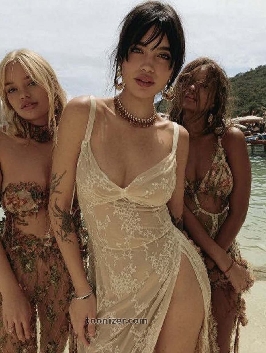 Three women in beachwear standing by the shore.