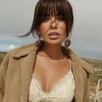 Woman in lace top with brown coat outdoors.