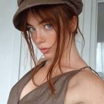 Person with hat and brown top poses indoors.