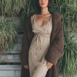 Stylish woman in elegant outfit by greenery wall.