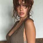 Woman wearing brown hat and dress poses indoors.