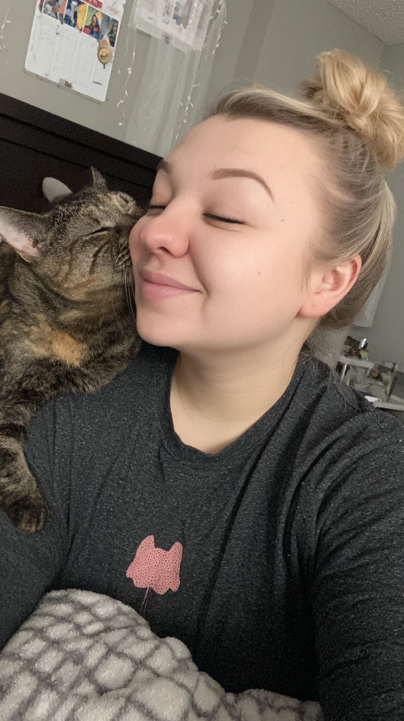 Smiling woman with affectionate cat on shoulder.