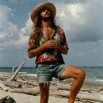 Man standing on beach with driftwood and backpack