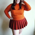 Woman in orange sweater and red pleated skirt