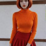 Woman with red bob wearing orange sweater and skirt