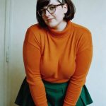 Person in orange sweater and green skirt indoors