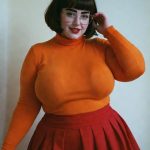 Woman in orange sweater and red skirt posing