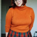 Woman in orange sweater and plaid skirt indoors