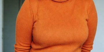 Woman in orange sweater and plaid skirt indoors