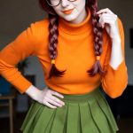 Woman in orange sweater and green skirt indoors