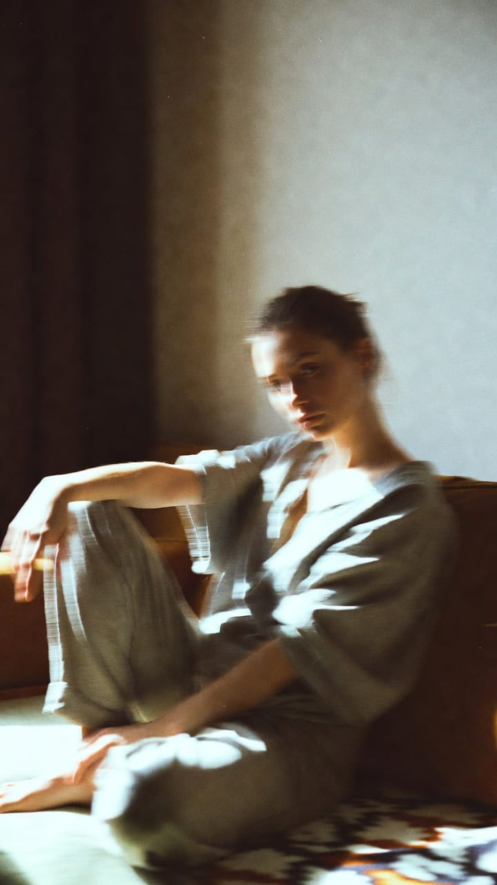 Woman sitting in sunlight by couch, soft blur