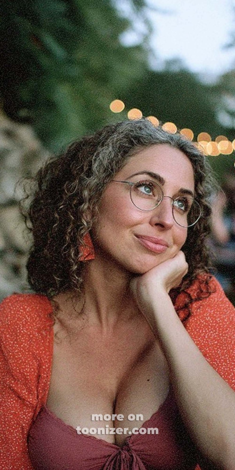 Woman with curly hair and glasses smiling outdoors